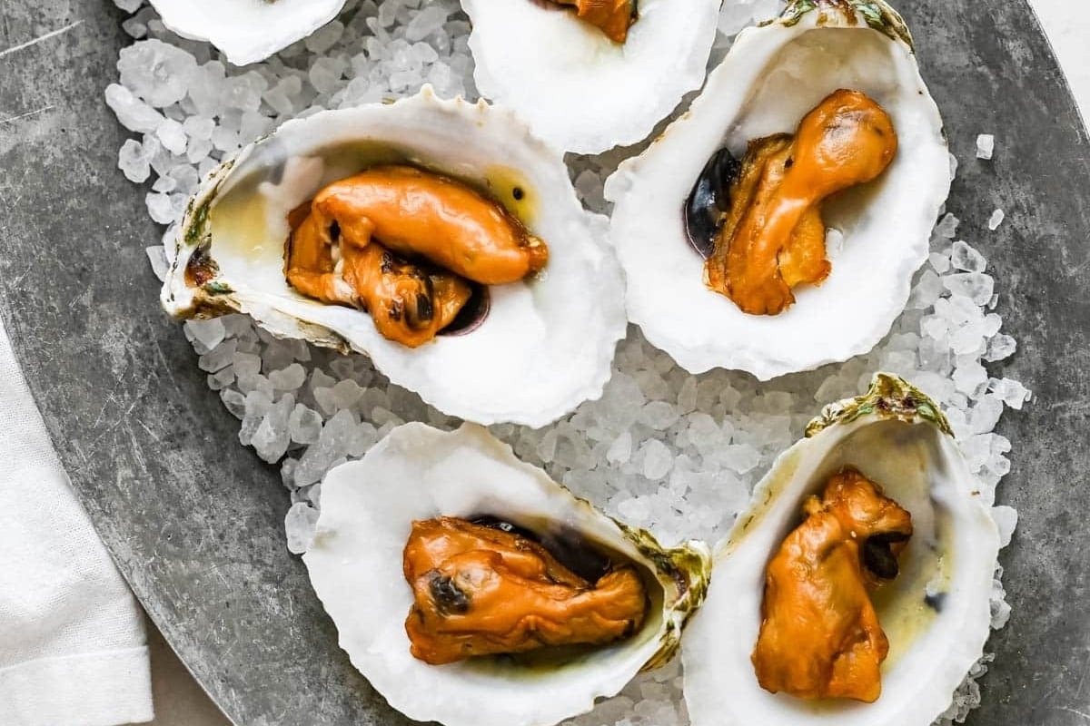 A plate of oysters on ice with orange sauce, perfect for a seafood feast.