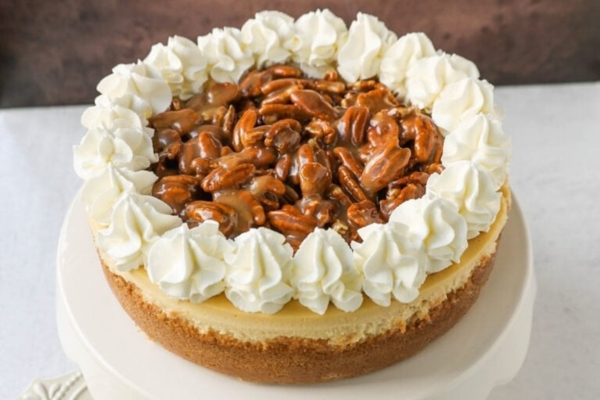 A decadent holiday cheesecake recipe featuring a luscious pecan filling, crowned with fluffy whipped cream and garnished with crunchy pecans.
