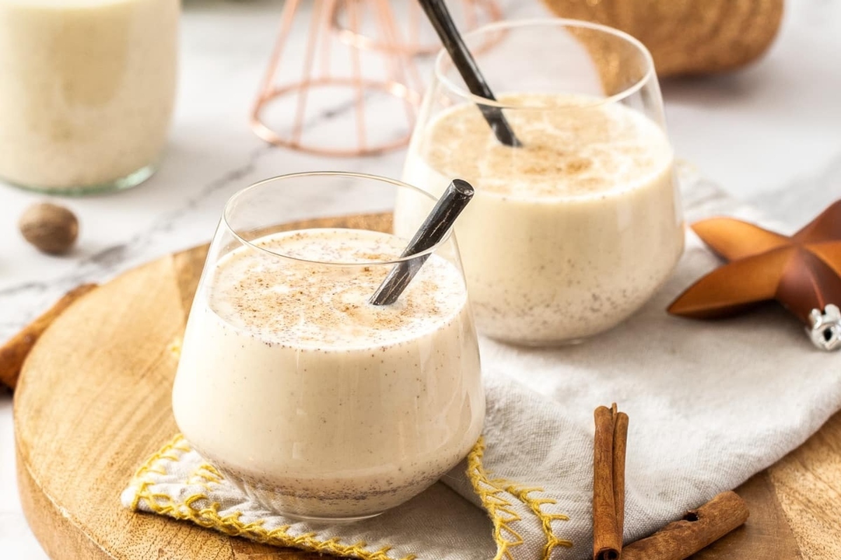 Two glasses of eggnog with cinnamon sticks on a wooden board.