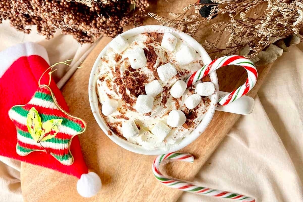 A warm cup of hot chocolate topped with fluffy marshmallows and adorned with festive candy canes.