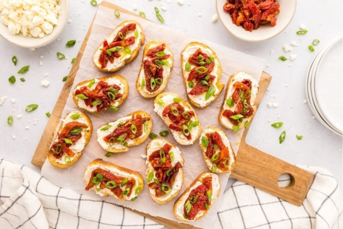 NYE appetizer: Roasted red pepper and goat cheese crostini on a cutting board.