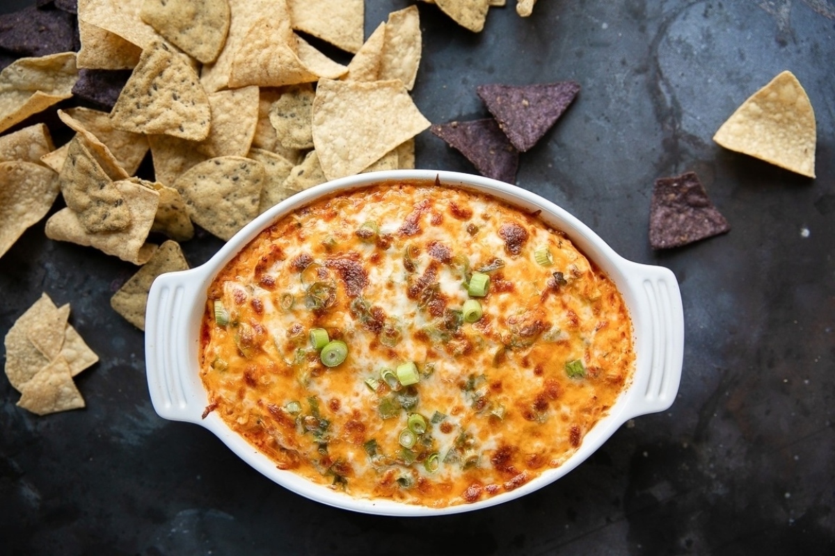 Cheesy buffalo chicken dip in a white bowl surrounded by tortilla chips, perfect for NYE appetizers.