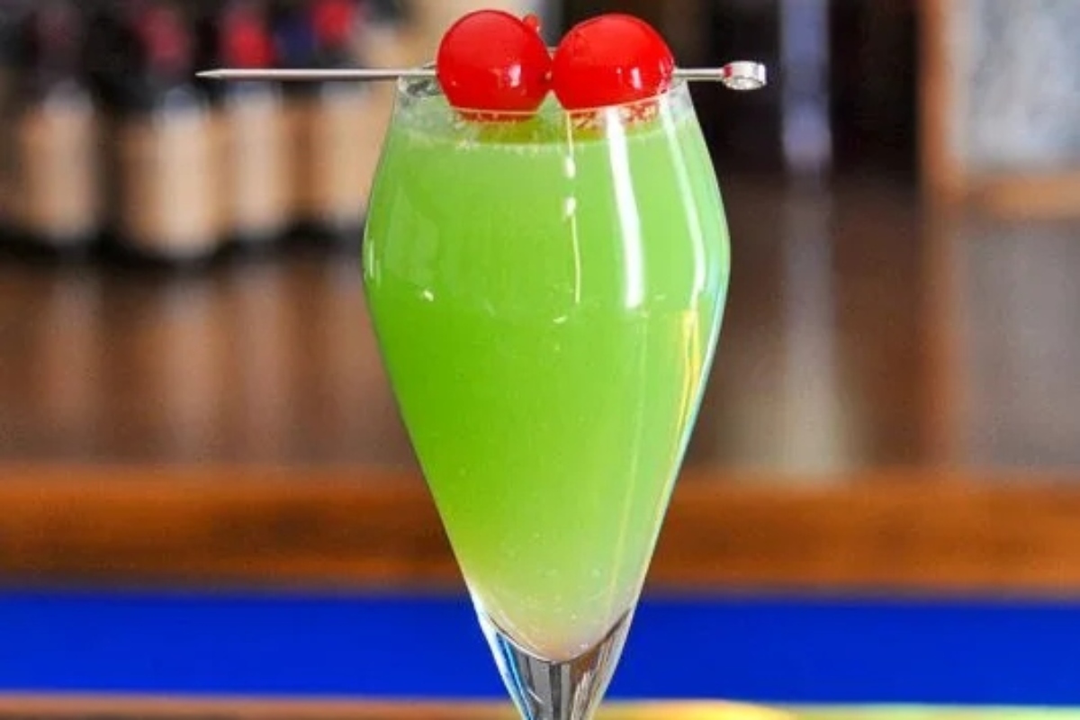 A glass of green Christmas drink with cherries on top.