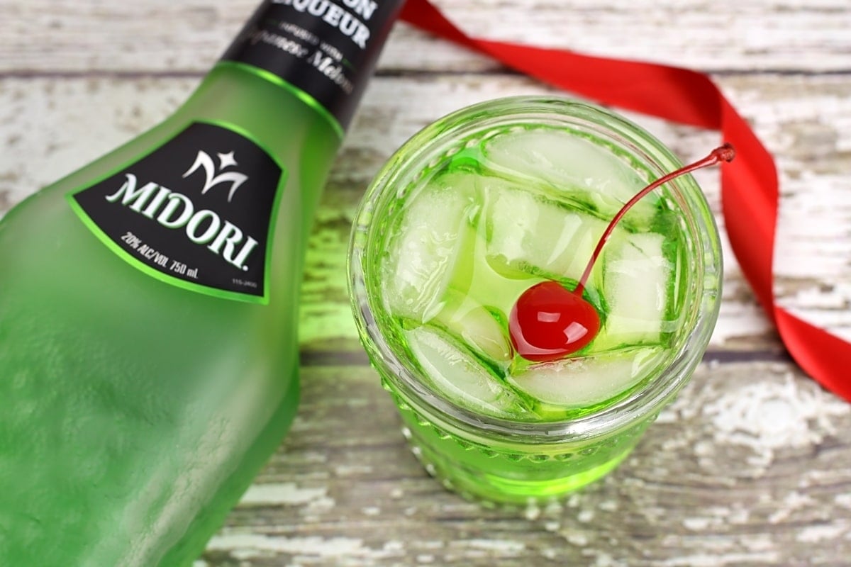 A bottle of green gin elevated with a festive cherry on top, perfect for Christmas drinks.