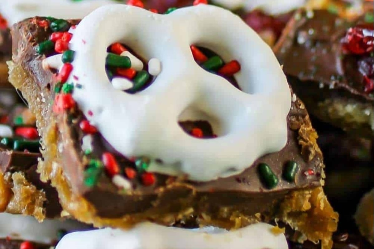 A close up of Christmas bark recipes including chocolate pretzel bars with icing and sprinkles.