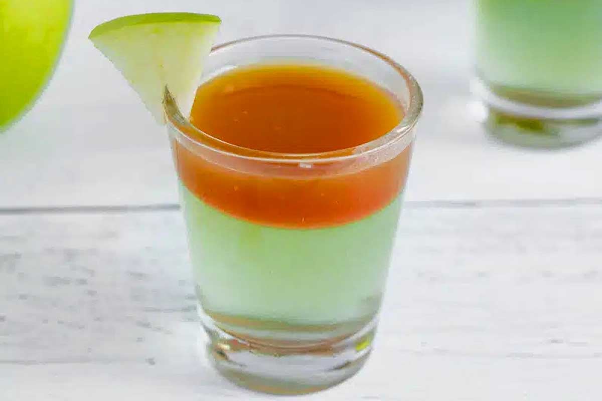 A refreshing shot of apple juice topped with a fresh slice of apple.
