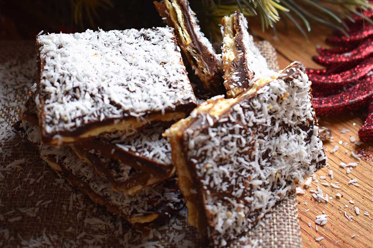 A stack of chocolate and coconut bars, resembling Christmas bark recipes, on a wooden table.