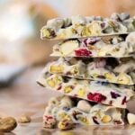 Stack of white chocolate bark with pistachios and dried cranberries on a wooden surface—perfect for trying out delicious Christmas bark recipes.