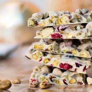 Stack of white chocolate bark with pistachios and dried cranberries on a wooden surface—perfect for trying out delicious Christmas bark recipes.