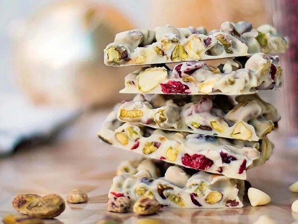 Stack of white chocolate bark with pistachios and dried cranberries on a wooden surface—perfect for trying out delicious Christmas bark recipes.