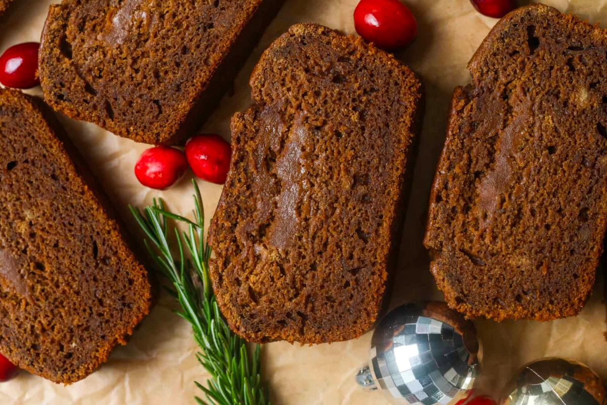 A delicious slice of chocolate gingerbread adorned with cranberries and sprigs of rosemary, perfect for a New Year's Eve party.