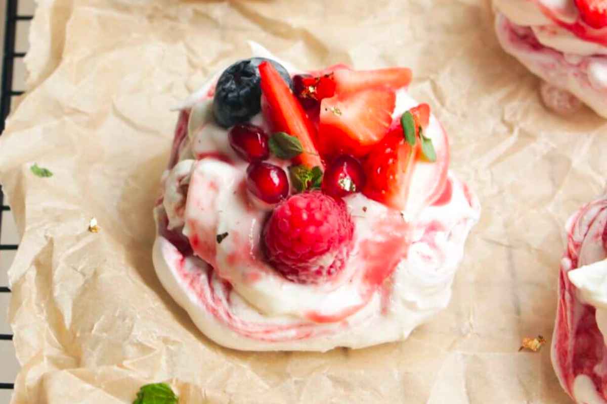 A tray of meringue desserts with berries and pomegranate.