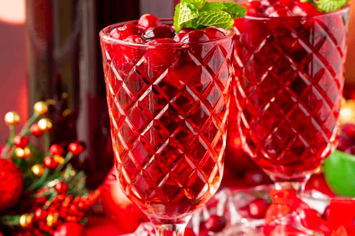 Two glasses of Christmas cocktails on a red background with cranberry juice.