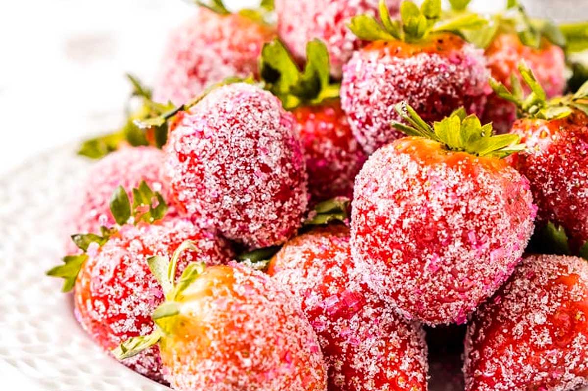 A pile of fresh strawberries coated with sugar crystals on a white plate—perfect for adding sparkle to your New Year's Eve desserts.