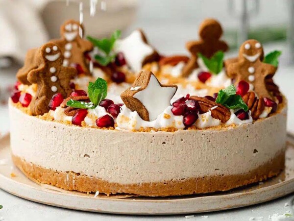 Celebrate the season with this festive holiday cheesecake recipe, topped with gingerbread cookies, whipped cream, pomegranate seeds, and mint leaves.