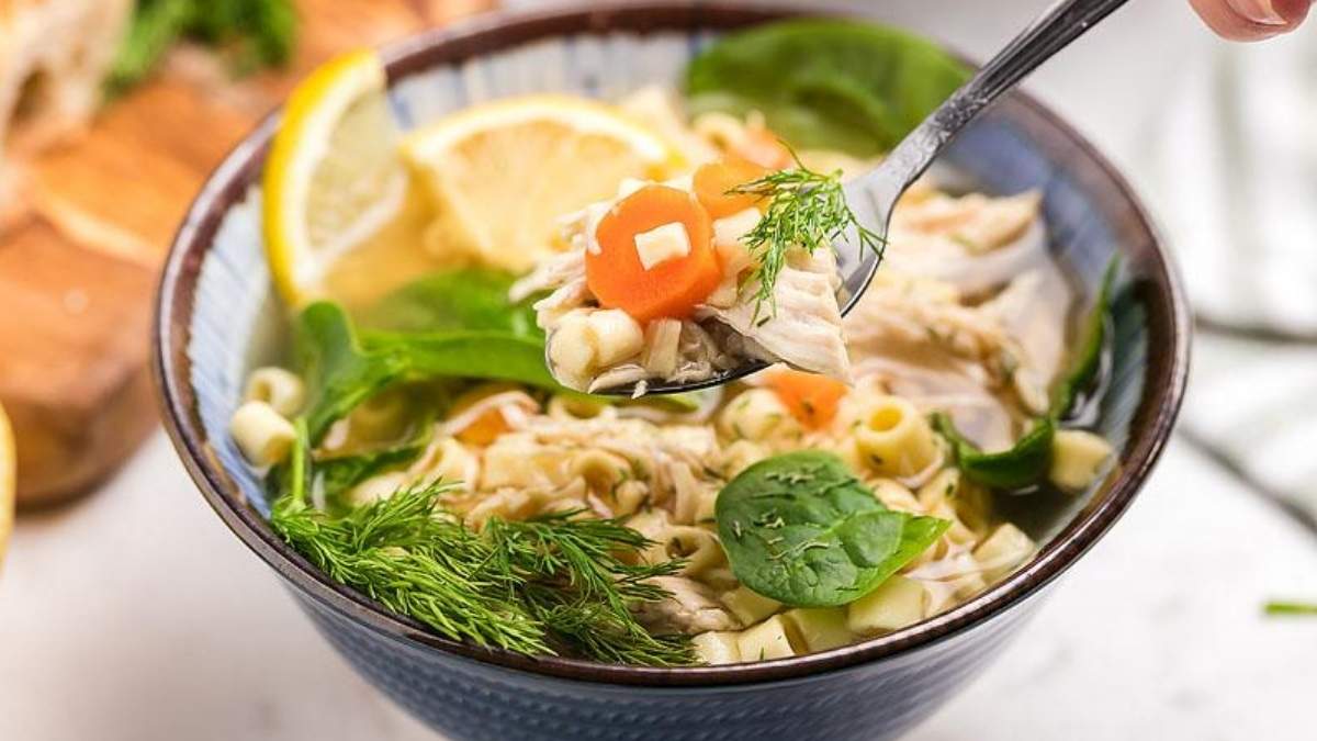 A bowl of chicken noodle soup with lemon and spinach.
