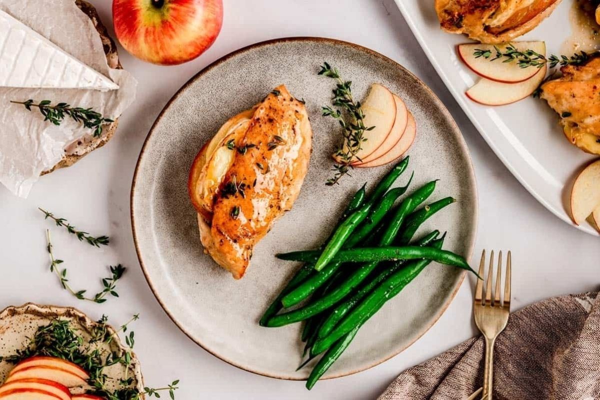 Grilled chicken breast with fresh thyme, green beans, and apple slices on a plate, with brie nearby—perfect for a cozy Valentine's Date Night Dinner.
