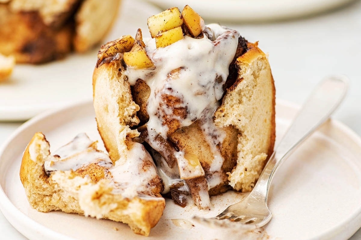 A sumptuous cinnamon roll, perfectly glazed with icing, served on a pristine plate along with a handy fork.