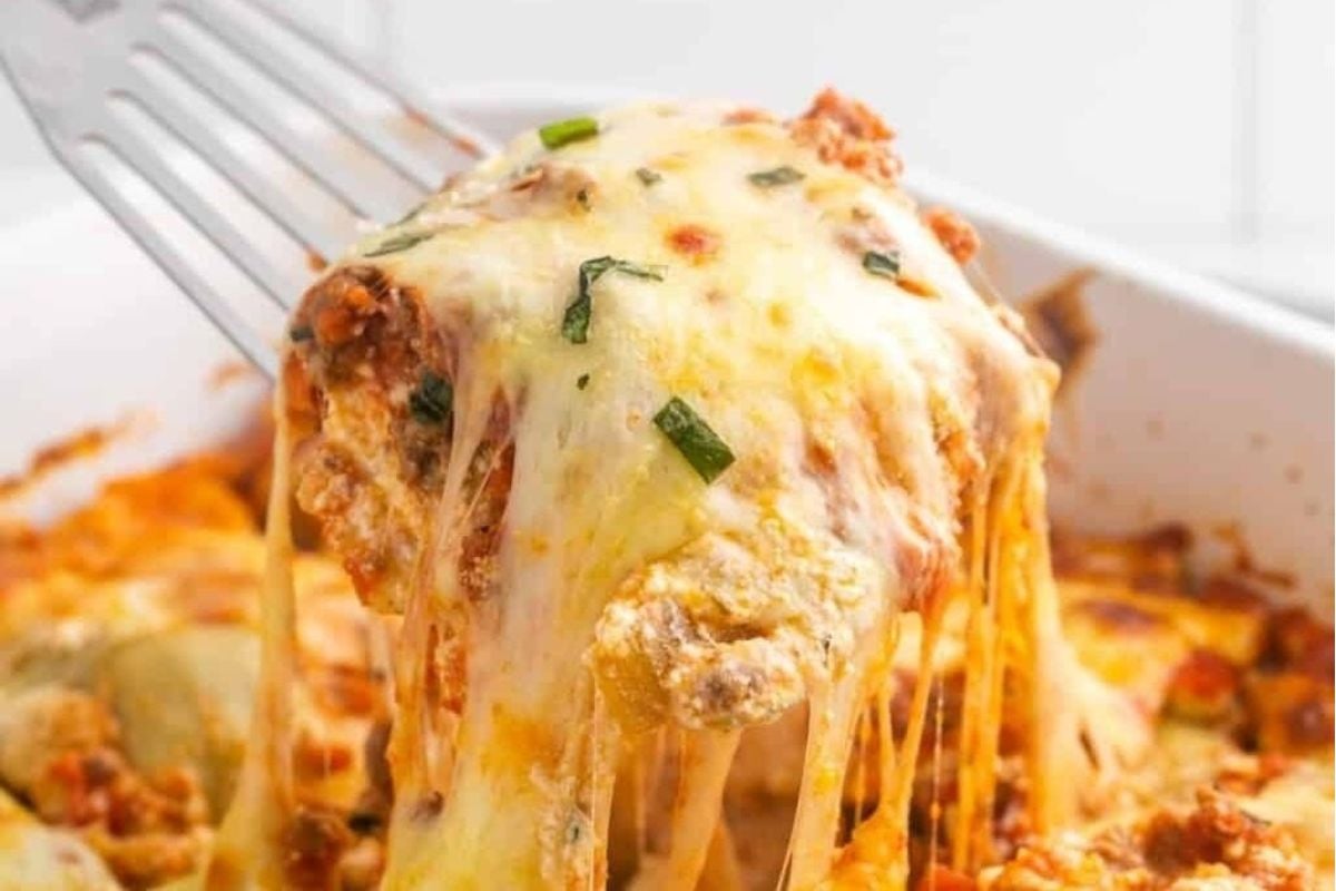 A fork is being used to take a piece of lasagna out of a casserole dish while cooking ravioli recipes.