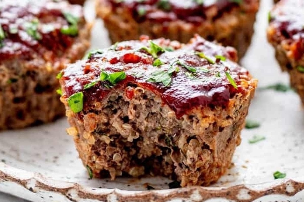 Individual savory meatloaf muffins topped with glaze and garnished with herbs on a speckled plate.