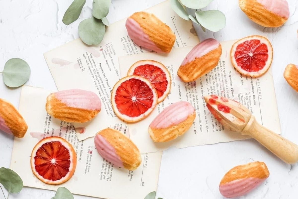 Blood orange macarons sit on a white table with eucalyptus leaves, perfect for fans of citrus recipes.