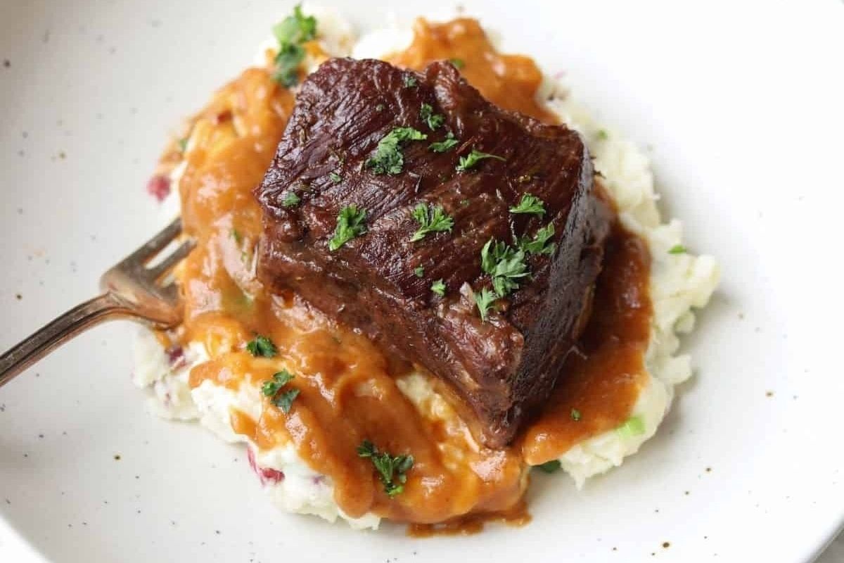 A perfect Valentine's Date Night Dinner: tender braised beef with rich gravy atop creamy mashed potatoes, elegantly garnished with chopped parsley.