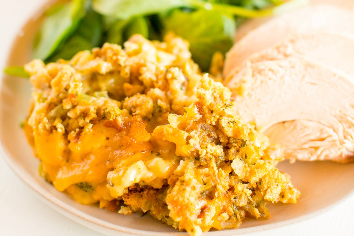 A plate of food with sliced turkey breast and a side of broccoli casserole topped with cheese.