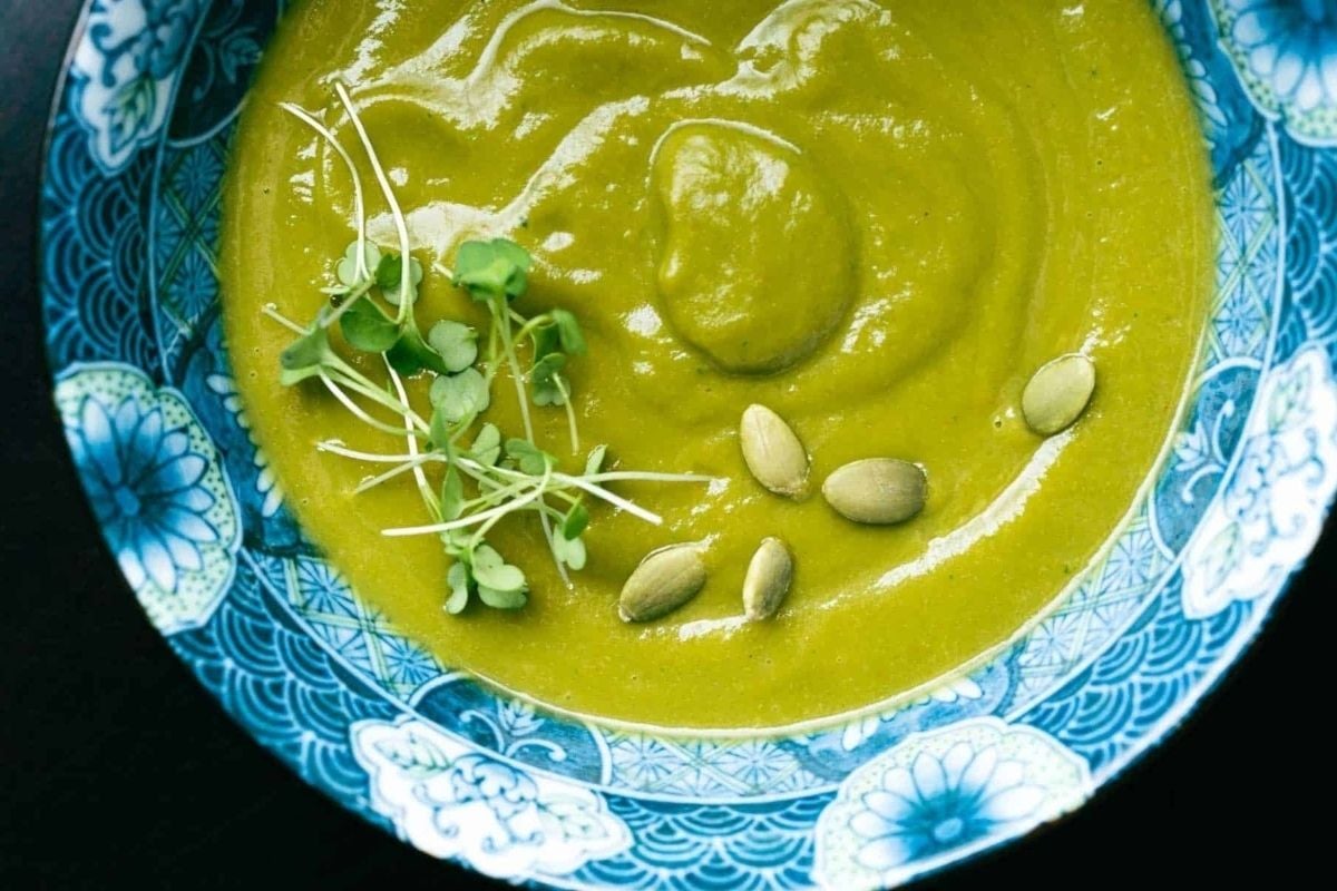A creamy bowl of green soup with sprouts and seeds.