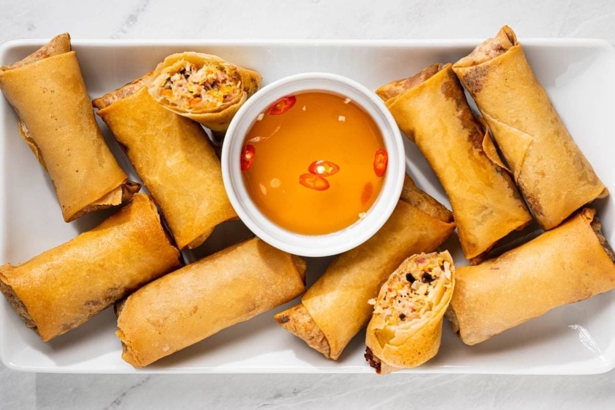 Golden fried spring rolls arranged around a bowl of dipping sauce with sliced red chili peppers—a festive favorite among Lunar New Year recipes.
