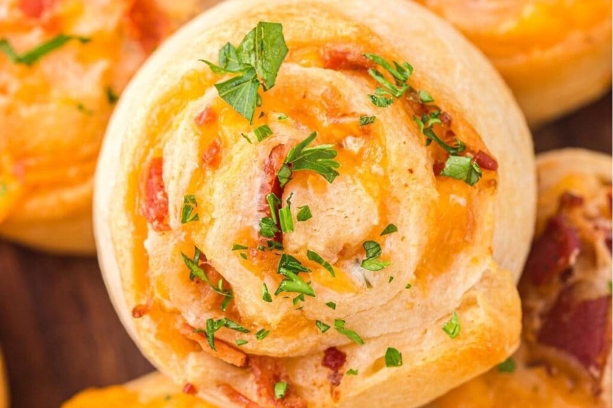 Close-up of a cheesy pizza roll, inspired by pinwheel recipes, topped with chopped parsley, showing golden, melted cheese and bits of bacon.