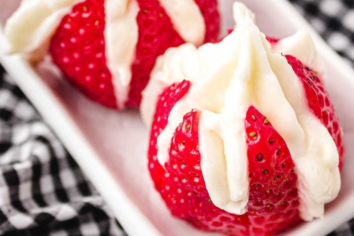 Two strawberries, Valentine's desserts, topped with white icing on a checkered tablecloth.