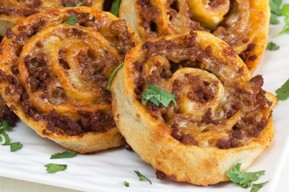 Close-up of savory pinwheels filled with ground meat and cheese, garnished with fresh cilantro on a white plate—a delicious example of creative pinwheel recipes.