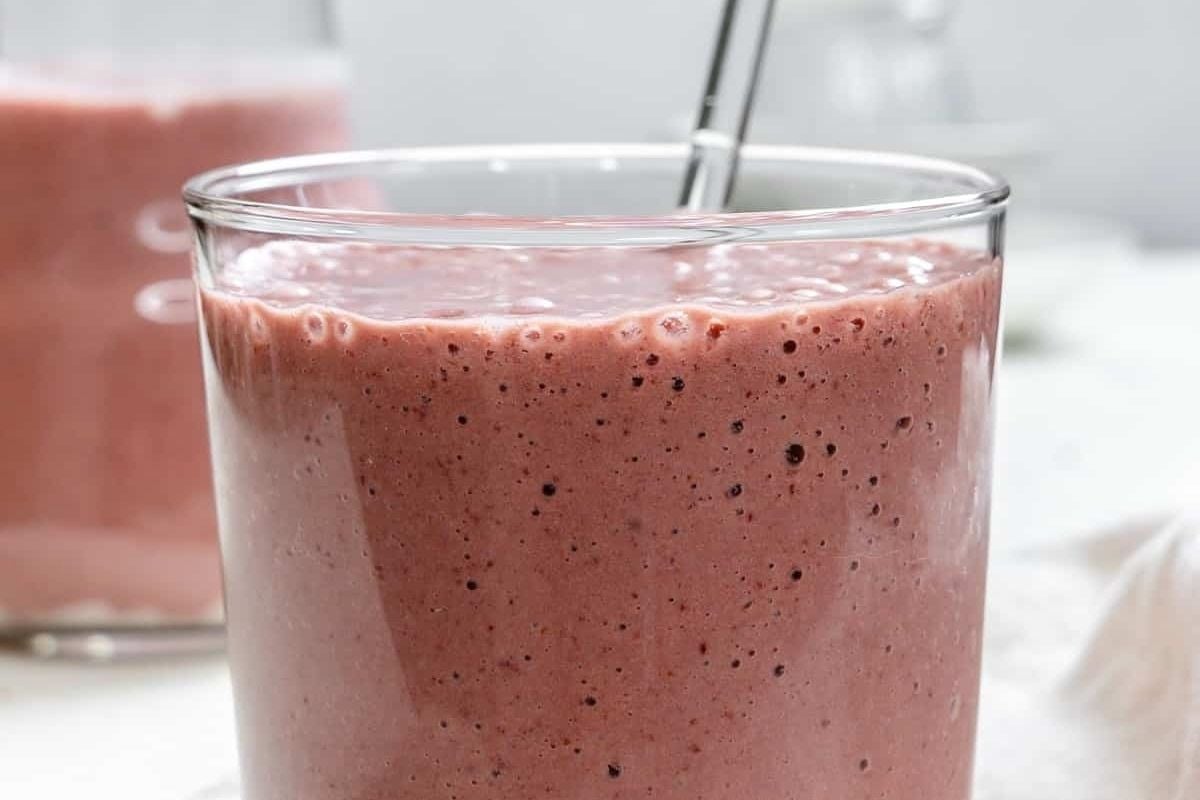 A glass of strawberry smoothie with a straw, featuring pinwheel recipes.
