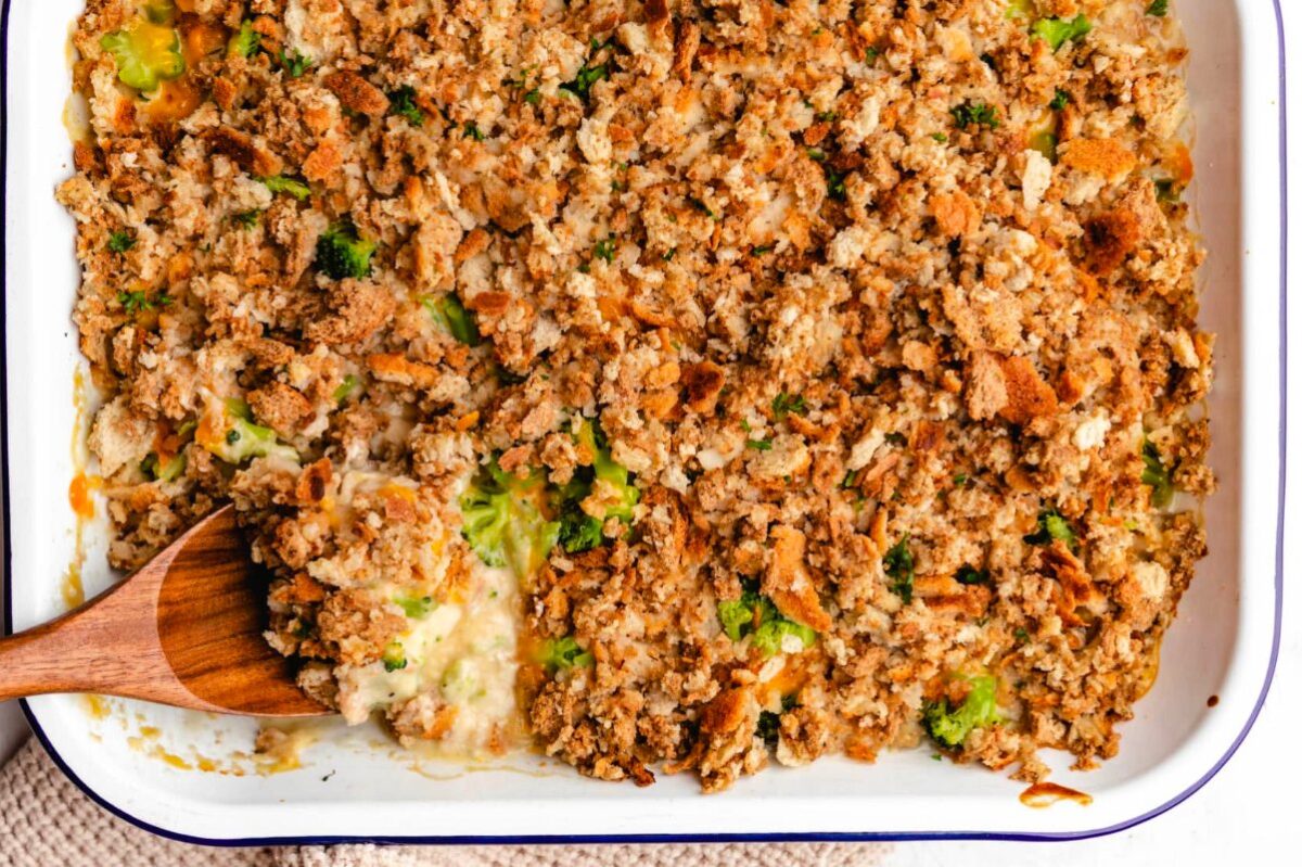 A casserole dish filled with turkey stuffing, featuring visible chunks of celery and herbs, with a wooden spoon.