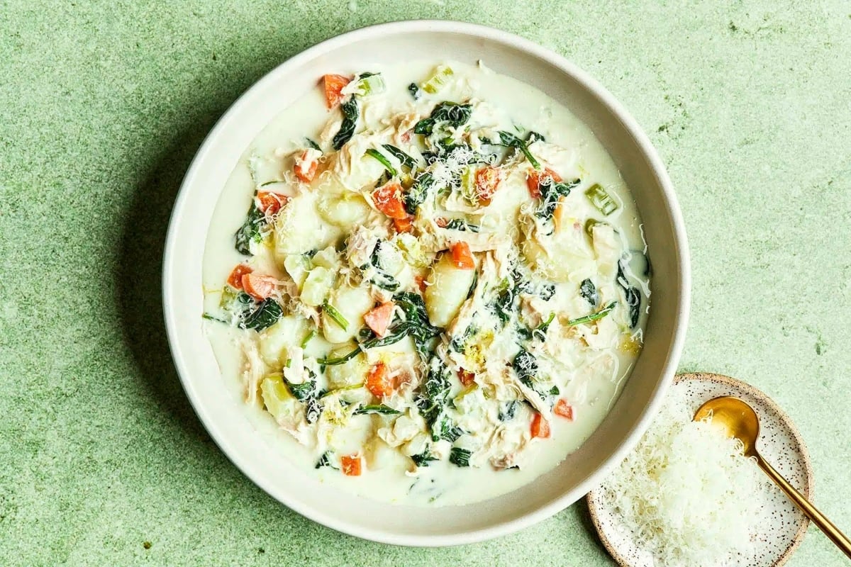 A bowl of chicken soup with vegetables on a green surface.
