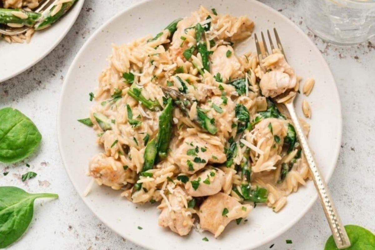 A plate of creamy orzo pasta with chicken, spinach, and asparagus, garnished with chopped parsley—a perfect choice for a cozy Valentine's Date Night Dinner.
