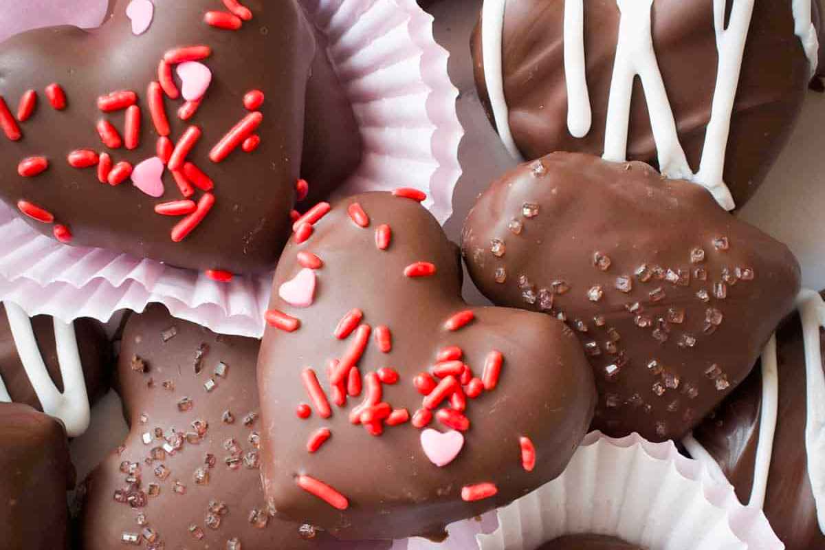 Heart-shaped chocolates decorated with sprinkles and icing, arranged in paper cups, make a sweet treat reminiscent of Valentine's Day cookies.