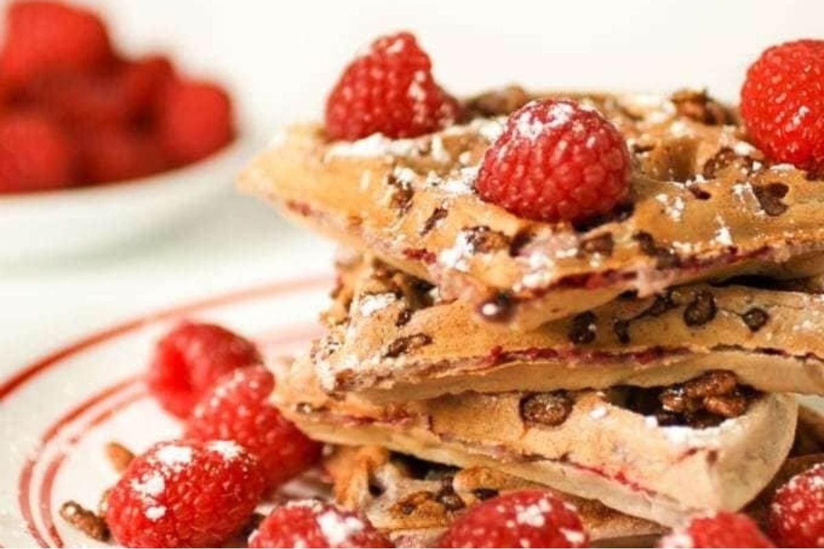 A stack of waffles with raspberries and powdered sugar, perfect for breakfast or brunch.