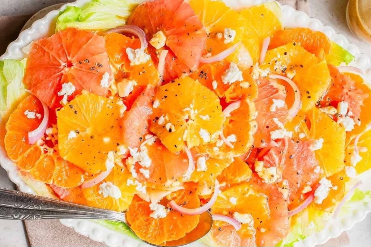 A citrus salad with feta cheese on a white plate.