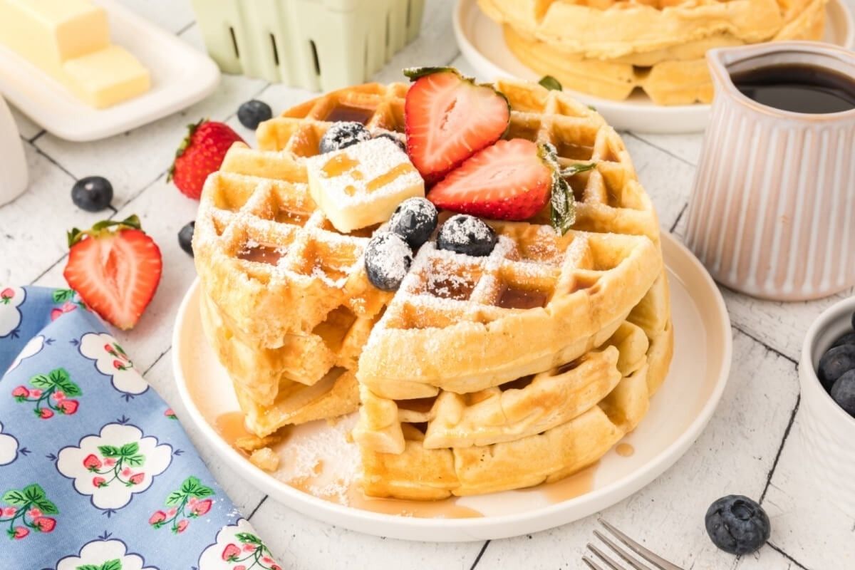 Delightful waffles adorned with succulent berries and drizzled with syrup on a rustic wooden table.