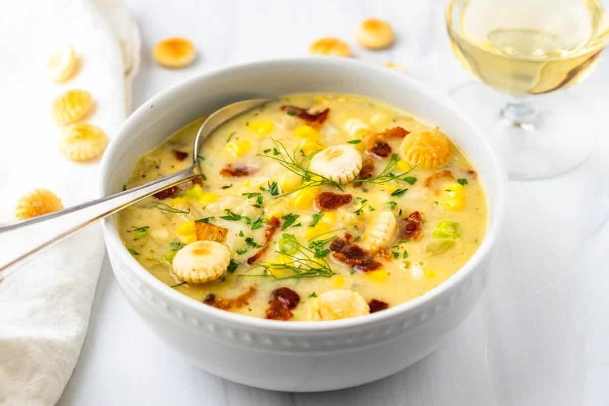 A delicious bowl of corn chowder with crackers and a glass of wine.
