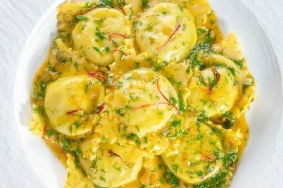 A plate of ravioli with a yellow sauce and herbs.
