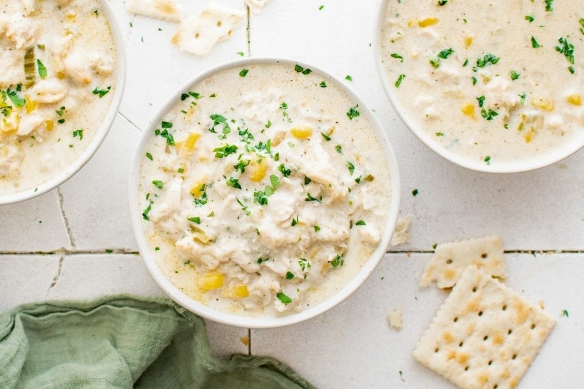 Three bowls of creamy corn chowder with crackers.