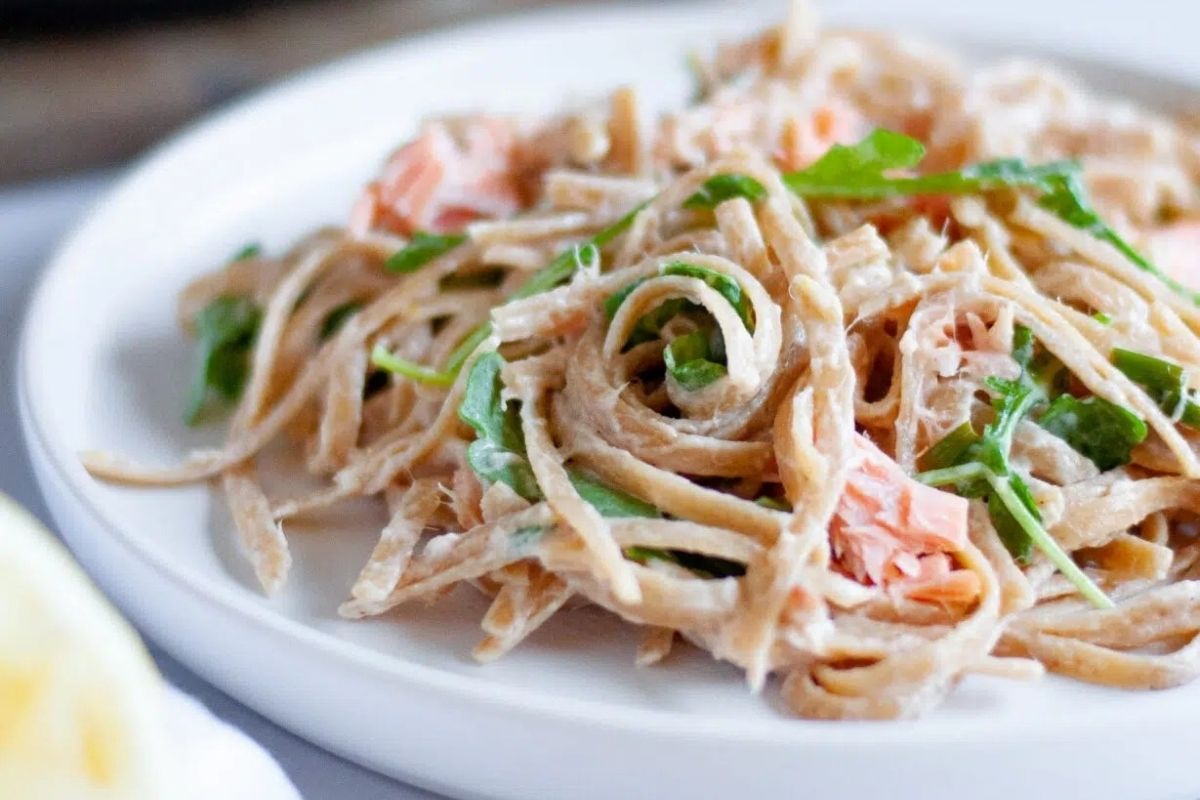 Whole wheat pasta with creamy sauce, salmon pieces, and fresh arugula on a white plate—perfect for a cozy Valentine's Date Night Dinner.