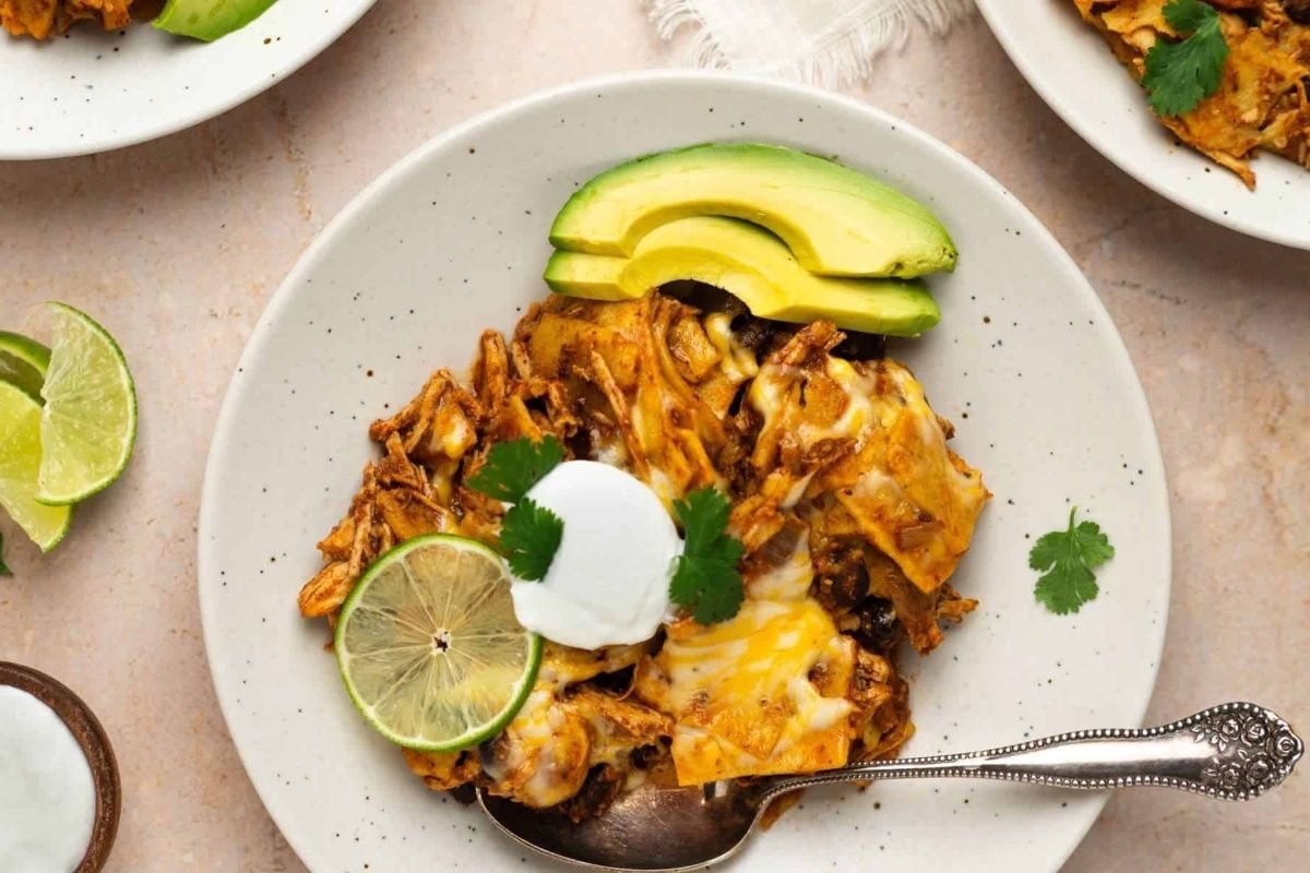 Wholesome Mexican chicken enchiladas on a white plate with sour cream and avocado, cooked in a slow cooker.