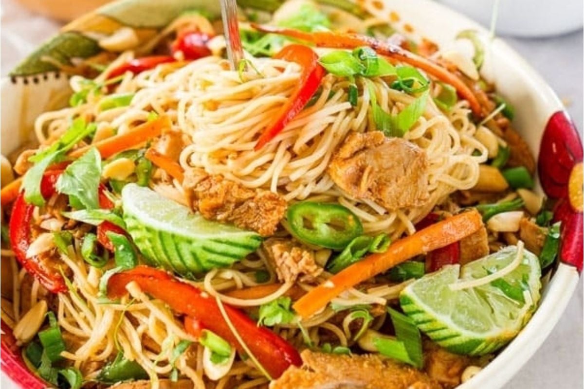 A bowl of noodle salad with slices of cucumber, lime, red bell pepper, green onions, carrots, and pieces of meat, garnished with cilantro&mdash;perfect for celebrating Lunar New Year recipes.