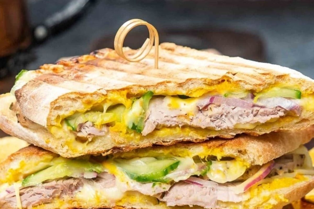 A grilled sandwich with pickle and vegetables on a plate.