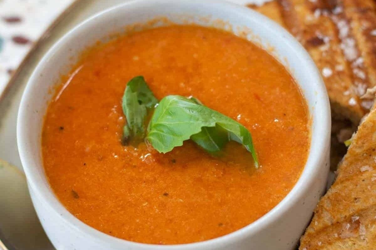 A bowl of tomato-based soup with bread and basil.
