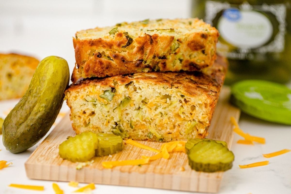 A loaf of bread with pickles and cheese on a cutting board.
