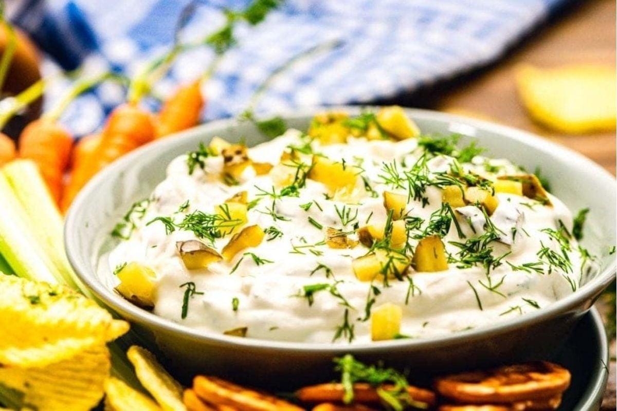 A bowl of dip with pickles and celery.